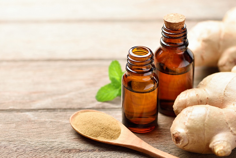 Ginger essential oil extract with powder and rhizome on wooden table.